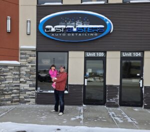 Owner Austin Marlow proudly stands with his daughter outside the welcoming Dustbusters Auto facility, highlighting the family-oriented spirit of their business.
