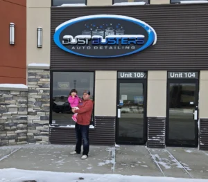 Owner Austin Marlow proudly stands with his daughter outside the welcoming Dustbusters Auto facility, highlighting the family-oriented spirit of their business.